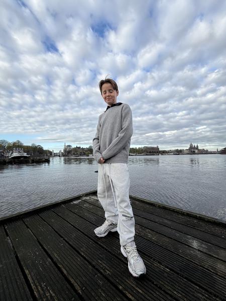 A young person stands on a dark wooden dock, looking peaceful with closed eyes, against a backdrop of a wide cloudy sky